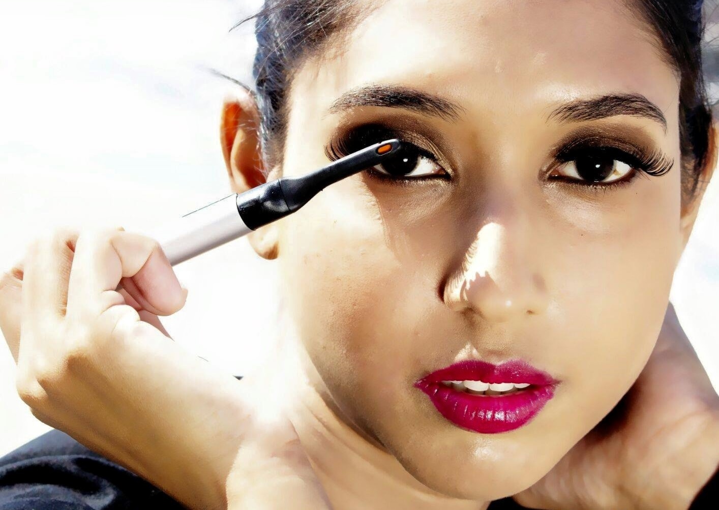 Makeup artist curling the lashes of a model wearing a smoked eye and berry lip