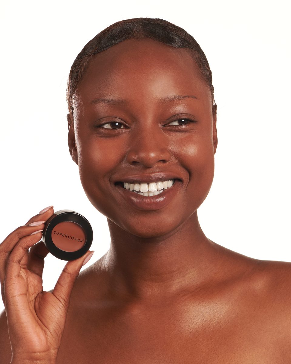 Model smiling and holding SUPERCOVER foundation